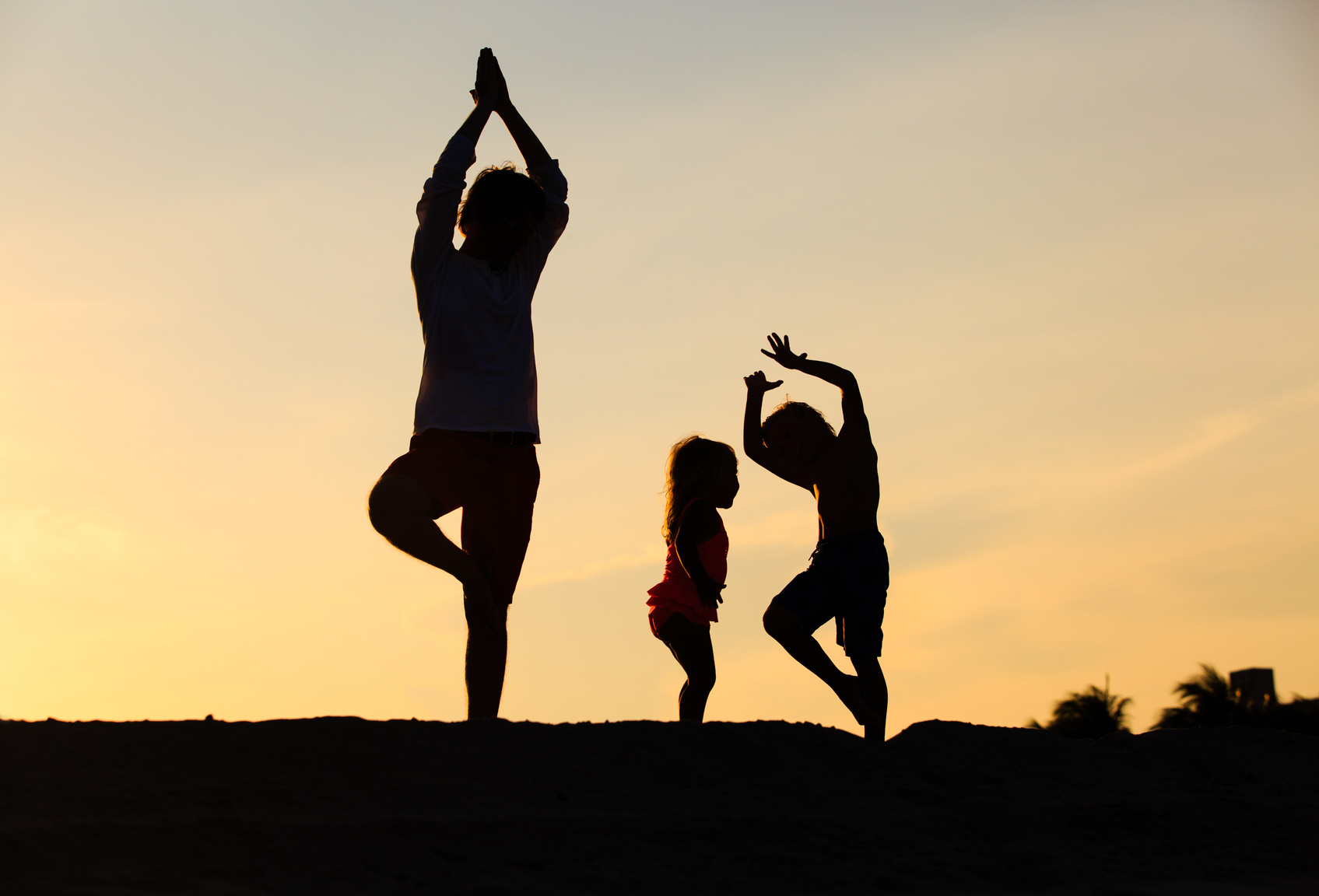 father with kids silhouettes doing yoga at sunset